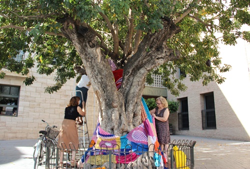 La concejala y la técnico de Participación Ciudadana quitan el ganchillo del árbol, junto a una participante del grupo "Tejiendo Beniel"